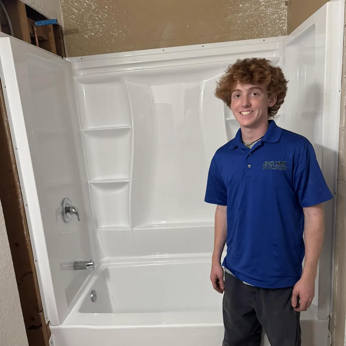 Young member of the Right Now Plumbing family in a company polo next to a freshly installed tub and shower